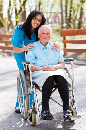 Beautiful doctor, nurse in blue coat walking a kind elderly lady in wheelchair in park.の写真素材