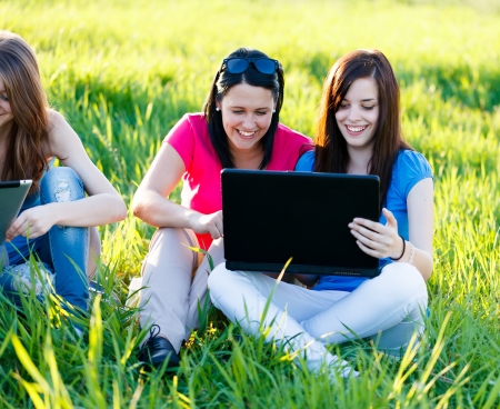 Girlfriends having fun outdoors using wireless internet on their laptops and tablet.の写真素材