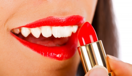 Lady smiling seductively while applying red lipstick.の写真素材
