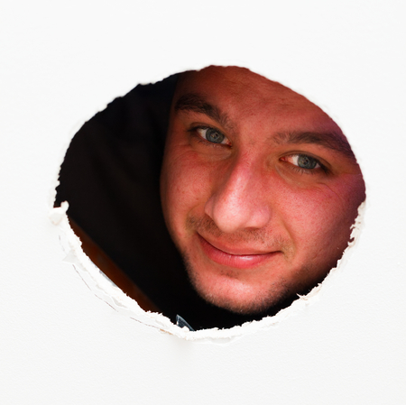 Kind man smiling looking through a cut hole.の写真素材