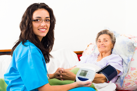 Kind nurse measuring elderly patient's blood pressure at home.の写真素材