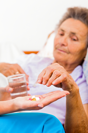 Elderly woman taking pills with glass of water.の写真素材