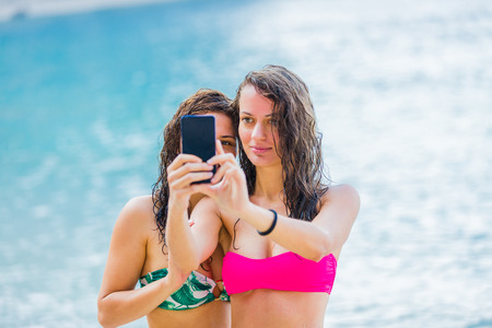 Young girls photographing themselves on the beach with a black smartphone.の写真素材