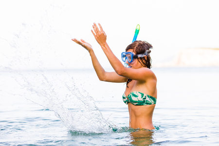 Playful woman splashing the seawater with snorkeling goggles and pipes on her head.の写真素材