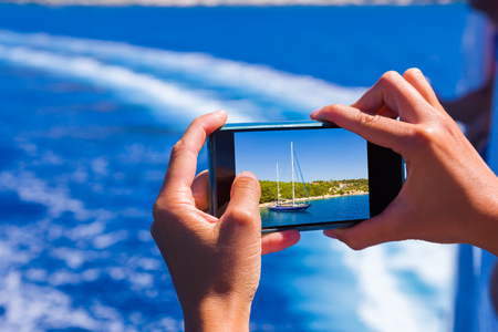 Young woman photographing the landscape from a moving ferry after departure.の写真素材