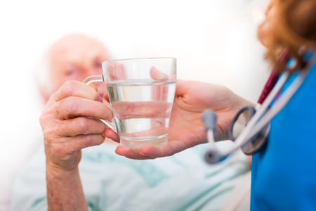 Elderly woman drinking water with the help of a nursing home caregiver.の写真素材