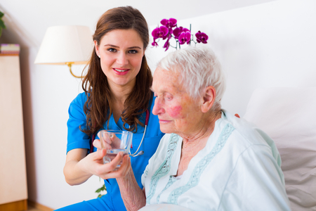 Caring nurse helping sick elderly woman to drink in bed in a nursing home.の写真素材