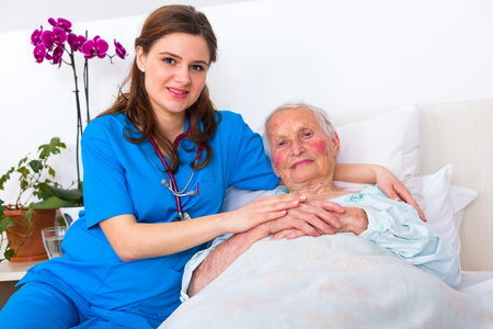 Elderly patient laying in bed in a nursing home with a caring young female doctor.の写真素材