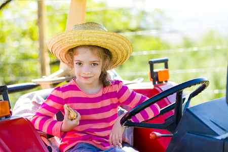 Beautiful little village girl eating on the tractor on fields.の写真素材