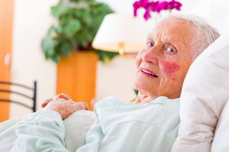 Elderly patient laying in bed in a nursing home waiting for the doctor.の写真素材