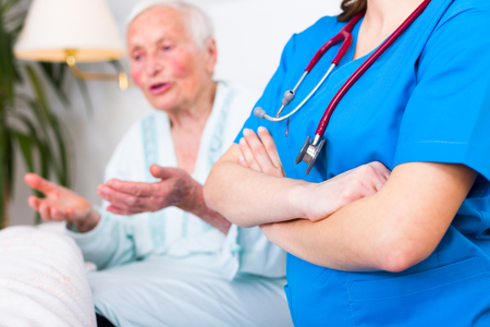 Confident geriatric doctor with stethoscope next to a talking elderly woman in hospital.の写真素材