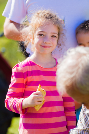 Little girl between grownups on the fields having a meal - a tasty sandwich.の写真素材