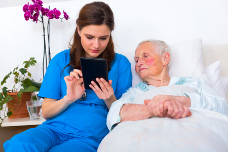 Caring nurse showing a digital tablet to an elderly woman in a nursing home.の写真素材