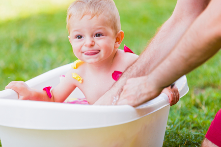 Little boy grimacing while his father washes him in the tub outdoors.の写真素材