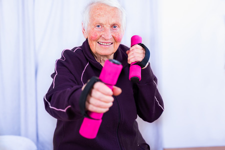 Senior woman training, doing fitness with pink weights at home.の写真素材
