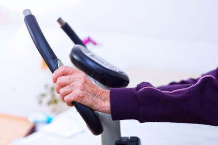 Elderly woman doing sport indoors on a staionary bicycle, training.の写真素材