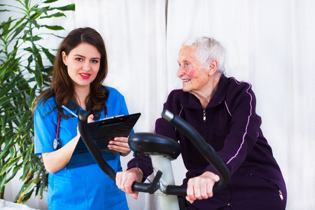Elderly woman doing sport effort while a kind geriatrician doctor is attending the event in a nursing home.の写真素材