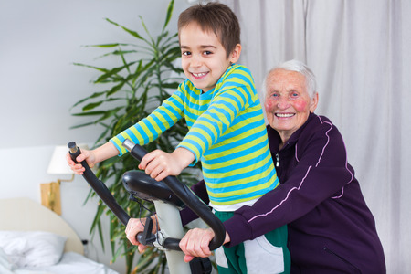 Grandmother training on stationary bike in the company of her grandson.の写真素材