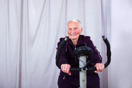 Senior woman on stationary bike indoors in a nursing home.の写真素材