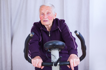 Senior woman on statoinary bike spinning, being tired because of training.の写真素材