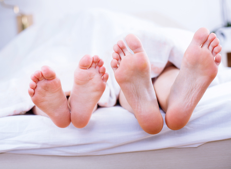 Parent and child feet in bed lolling out from under the duvet.の写真素材