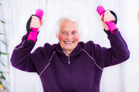 Senior woman training, doing fitness with pink weights at home.の写真素材