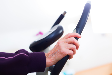 Close-up of an elderly woman's hands doing sport, training on a stationary bicycle indoors in the nursing home.の写真素材