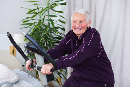 Senior woman on stationary bike indoors in a nursing home.の写真素材