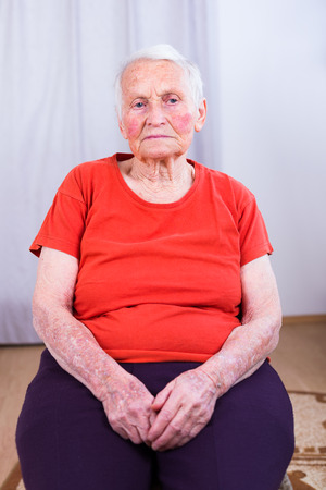 Sad and sick senior woman sitting on a chair in her room.の写真素材
