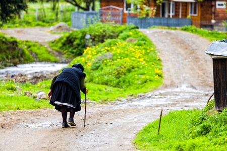 Elderly woman with walking stick going towards her home on the road of the village.の写真素材