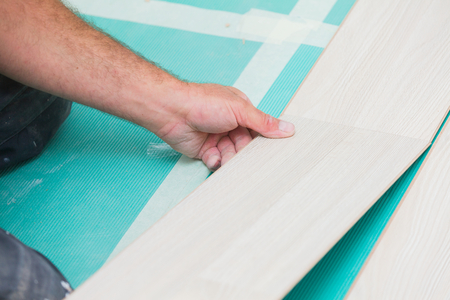 Handyman laying down laminate flooring boards while renovating a house.の写真素材