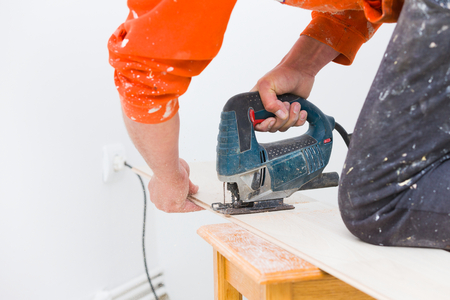 Handyman cutting wooden laminate floor board to make it fit on the flooring with electrical saw.の写真素材