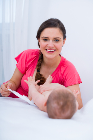 Smiling beautiful young mother putting on diapers for her baby.の写真素材