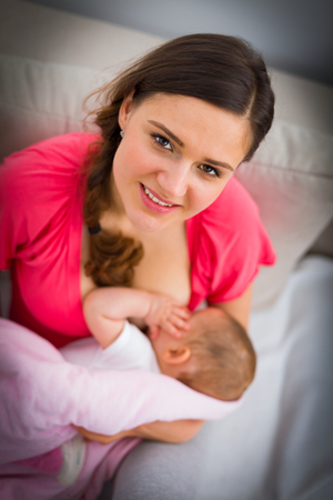 Beautiful young woman brestfeeding her child at home.の写真素材