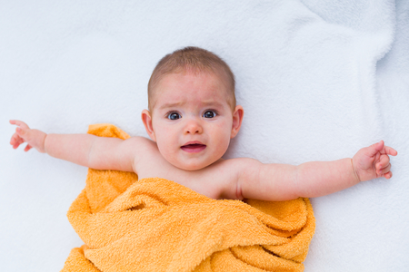 Beautiful baby laying on bed, making funny face to the camera.の写真素材