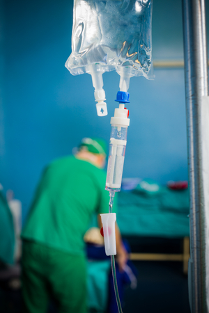 Focus on the perfusion bag with nutritions and plysiologycal saline, doctor working in the background.の写真素材