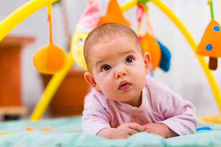 Cute little baby looking upwards, laying on her little home playground.の写真素材