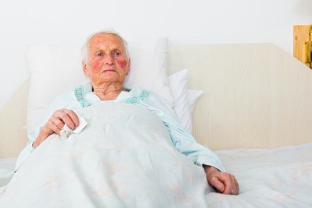 elderly woman laying sad in bed waiting for doctor.の写真素材