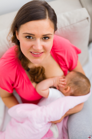 Beautiful happy mother breastfeeding her child at home.の写真素材