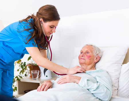 Young nurse examining an elderly woman with stethoscope, lustening to the lung and heart sounds.の写真素材