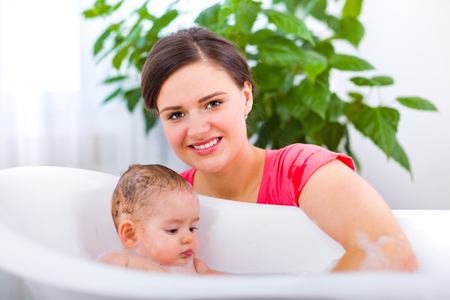 Mother washing her little baby in a plastic bathtub having fun.の写真素材