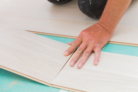 Handyman's dusty hands laying down laminate wood flooring boards, mounting them together with great care.の写真素材