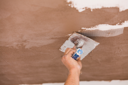 Construction worker skim coating the ceiling after the application of fiberglass net.の写真素材