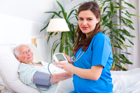 Kind carer measuring the blood pressure of a happy elderly woman in bed in the nursing home.の写真素材