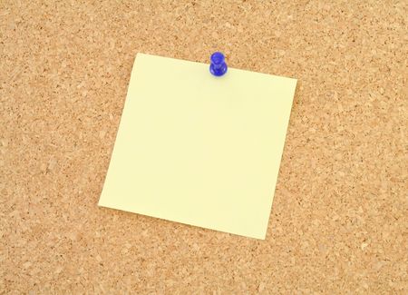 Corkboard with blank yellow notepaper and blue pushpinの写真素材