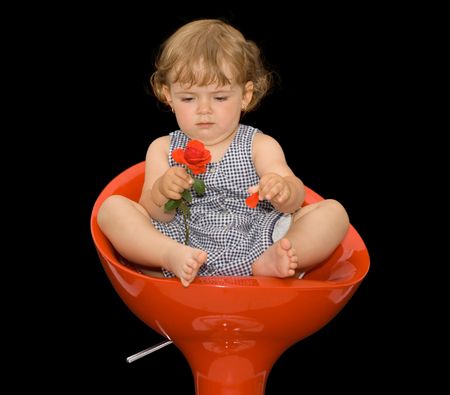 Little girl on a red swivel chair playing with a rose - he loves me, he loves me not - isolated on black - focus on the eyesの写真素材