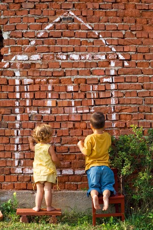 Two children drawing fantasy home on a brick wall - real estate conceptの写真素材