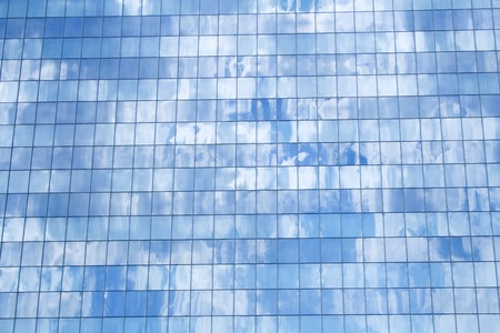 Glass building detail reflecting the fluffy clouds in the blue sky - background