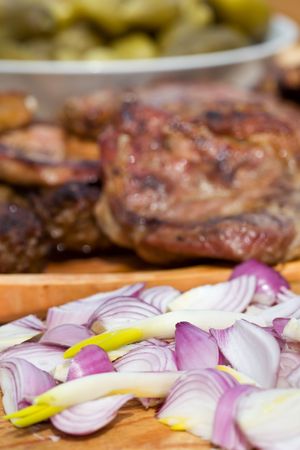 Onions, grilled or barbecued pork meat on wooden plate and pickled gherkins closeup - focus in the frontの写真素材