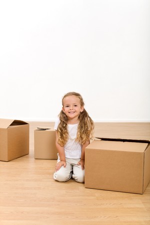 Laughing little girl sitting among cardboard boxes in her new home